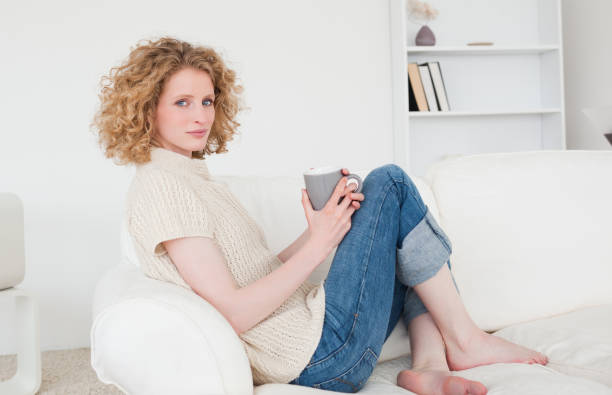 istock Charming blonde female enjoying a cup of coffee while sitting on a sofa 828168812
