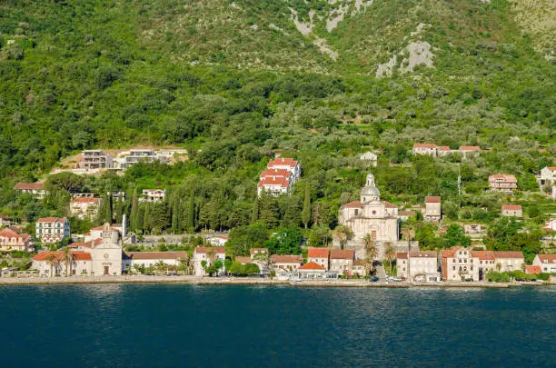Prcanj - a small town along the Bay of Kotor, Montenegro. A part of the waterfront, that consists of a long line of stone villas and churches, separated by gardens and olive orchards, with the baroque Birth of Our Lady church to the right.