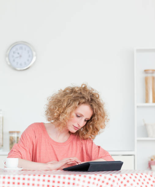 istock Charming blonde woman relaxing with her tablet while sitting in the kitchen 828212322