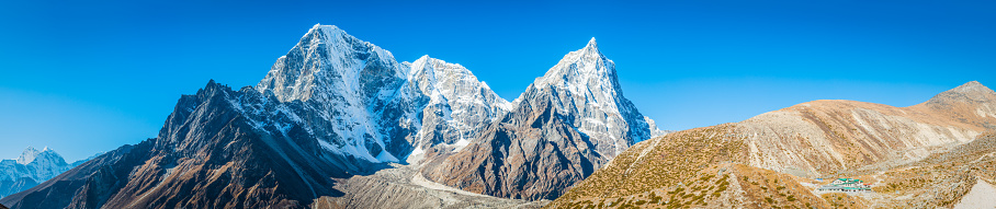 The snow capped summits of Tawoche (6542m) and Cholatse (6440m) overlooking Sherpa village teahouse lodges high in the Himalayan mountains of the Everest National Park, Nepal.