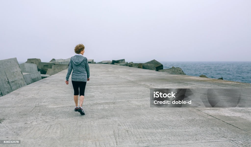 Back view of woman walking by sea pier Back view of unrecognizable woman walking outdoors by sea pier Exercising Stock Photo