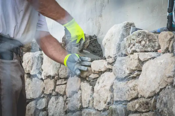 Photo of worker rides a stone wall on a traditional renovation site