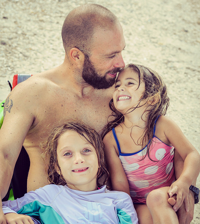 Little girls and their father relax in beach wear on the beach, real people, really happy