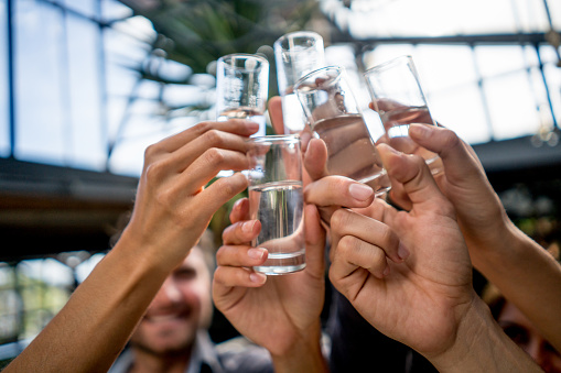 Close-up on a group of friends toasting with shots at a bar - lifestyle concepts
