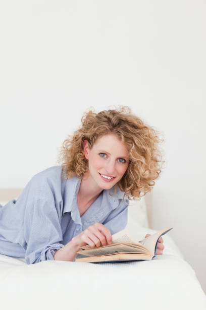 istock Attractive blonde woman reading a book while lying on her bed 828245264
