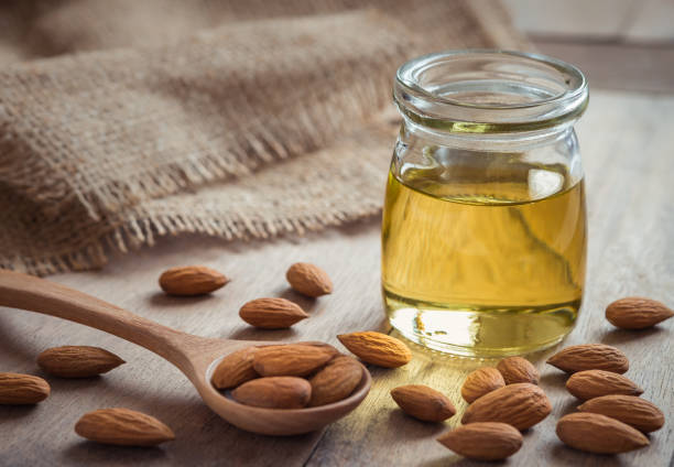 huile d’amande dans la bouteille en verre et amandes sur table en bois - huile de massage photos et images de collection