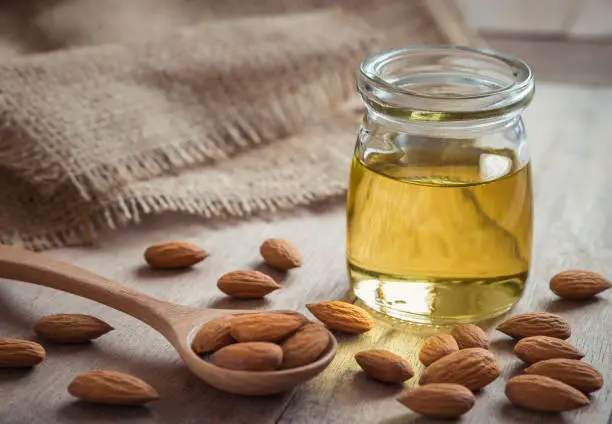 Photo of Almond oil in glass bottle and almonds on wooden table