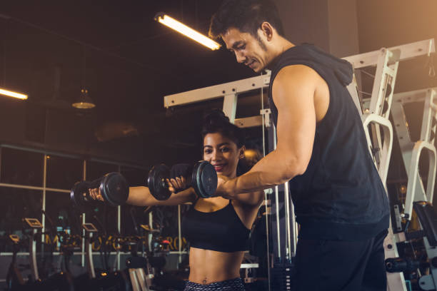istock Personal training man helping women's arms to pull up dumbbell for exercise at indoor gym. 828315162