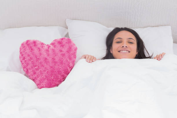 istock Woman lying in bed next to a fluffy heart pillow 828353164