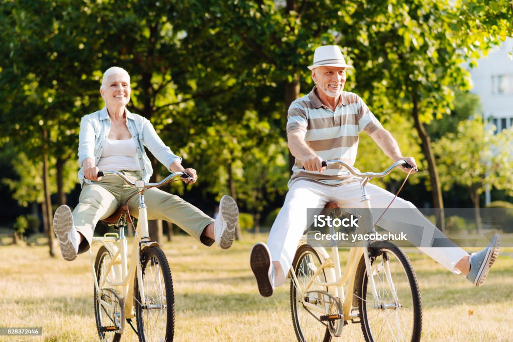 Joyful woman feeling happiness while cycling Like little children. Positive male person holding handle bar and keeping smile on his face while looking forward Aging Process Stock Photo
