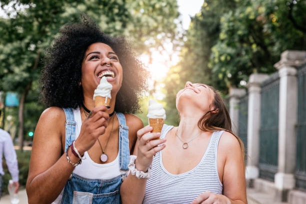 красивые женщины едят одно мороженое на улице. - couple young adult african descent multi ethnic group стоковые фото и изображения