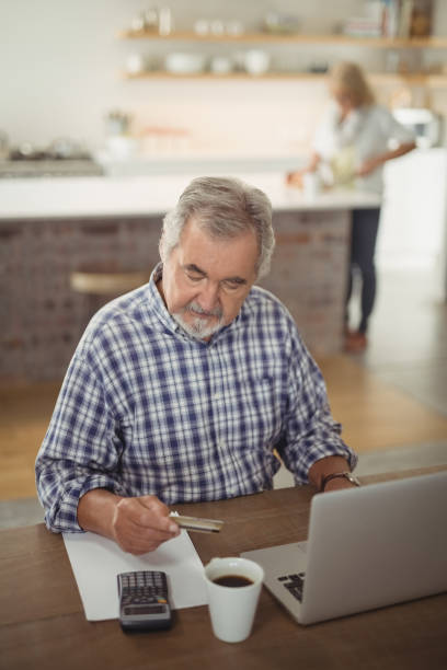 istock Senior man paying bills online on laptop in kitchen 828448096