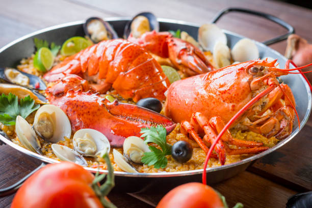 Paella with fresh lobster, clams, mussels and squid Gourmet seafood Valencia paella with fresh langoustine, clams, mussels and squid on savory saffron rice with peas and lemon slices, close up view conceptional stock pictures, royalty-free photos & images
