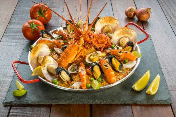 Paella with fresh lobster, scallops, mussels and prawn Gourmet seafood Valencia paella with fresh langoustine, clams, mussels and squid on savory saffron rice with prawn, scollops, mussels and lime slices, close up view conceptional stock pictures, royalty-free photos & images