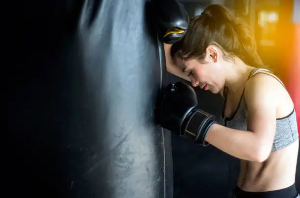 Photo of sexy fighter girl in gym with boxing bag. Long hair woman fitness ufc model