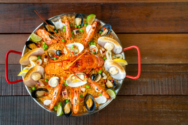 Paella with fresh lobster, scallops, mussels and prawn Gourmet seafood Valencia paella with fresh langoustine, clams, mussels and squid on savory saffron rice with prawn, scollops, mussels and lime slices, close up view conceptional stock pictures, royalty-free photos & images