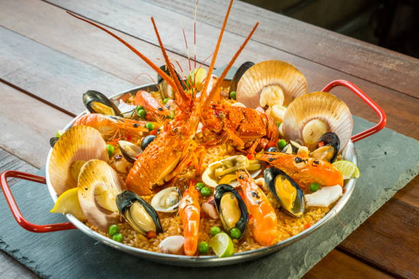 Paella with fresh lobster, scallops, mussels and prawn Gourmet seafood Valencia paella with fresh langoustine, clams, mussels and squid on savory saffron rice with prawn, scollops, mussels and lime slices, close up view conceptional stock pictures, royalty-free photos & images