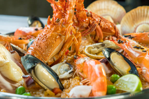 Gourmet seafood Valencia paella with fresh langoustine, clams, mussels and squid on savory saffron rice with prawn, scollops, mussels and lime slices, close up view