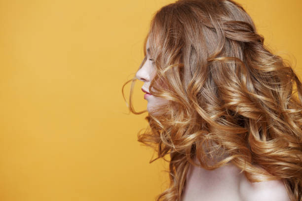 Beautiful redheaded girl with luxurious curly hair. Portrait in profile. Free space left. Studio portrait on yellow background. stock photo