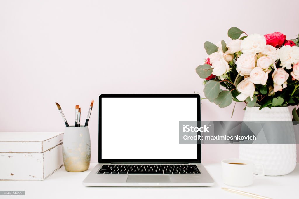 Home office desk with blank screen laptop Home office desk with blank screen laptop, beautiful roses and eucalyptus bouquet, white vintage casket in front of pale pastel pink background. Blog, website or social media concept . Desk Stock Photo
