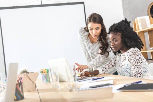 istock focused businesswomen using laptop together at workplace 828476524
