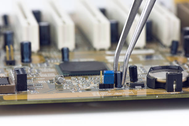 Tweezers Holding And Assembling Black Microchip On Computer Motherboard CloseupTweezers Holding And Assembling Electrolytic Capacitors And Conductors On Computer Motherboard Closeup