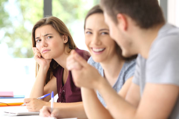 Couple in love and jealous classmate watching them Couple in love and a jealous classmate watching them in a classroom envy stock pictures, royalty-free photos & images