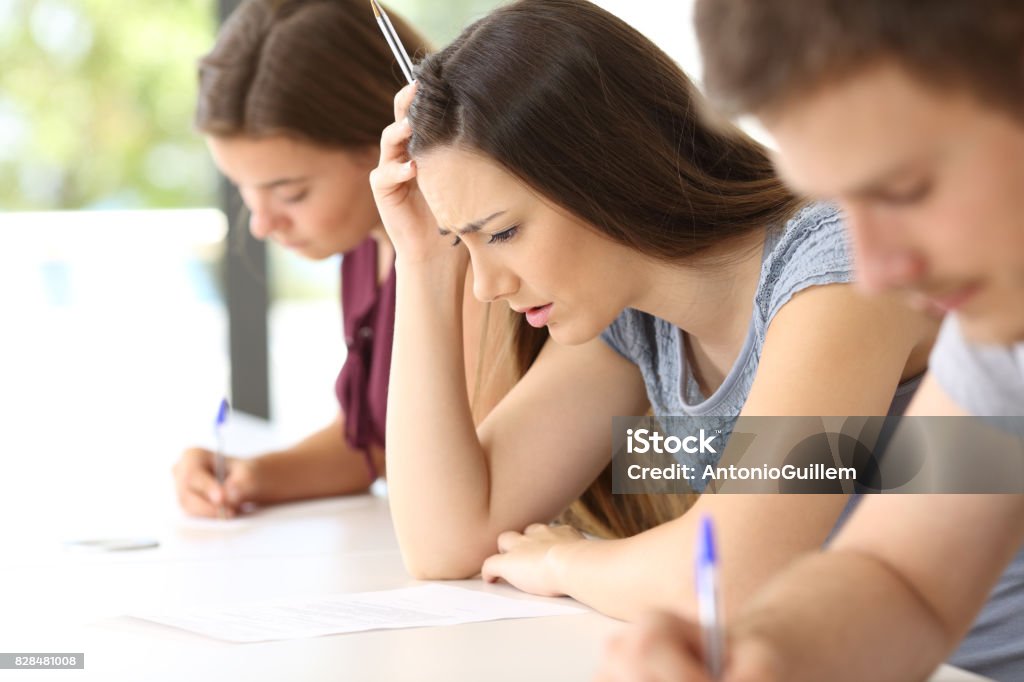 Worried student trying to do a difficult exam Side view of a worried student trying to do a difficult exam in a classroom Educational Exam Stock Photo