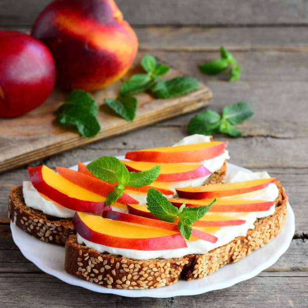 istock Breakfast sandwiches with soft cheese, fresh nectarines slices and mint. Healthy protein sandwiches on a plate and on vintage wooden table. Rustic style. Closeup 828482108