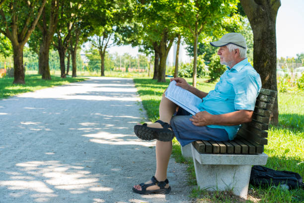 istock Side view of Senior reading a book while sitting on bench in shadow on The Trail of Remembrance and Comradeship in Ljubljana, Slovenia 828484628