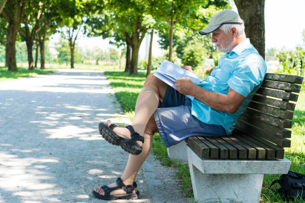 vista lateral de senior leyendo un libro sentado en la banca en la sombra en el camino de la memoria y la camaradería en ljubljana, eslovenia - bench mountain park sitting fotografías e imágenes de stock