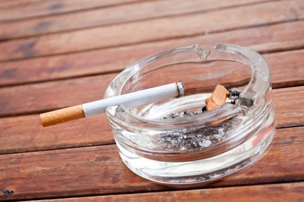 cigarette on the edge of the  ashtray on wooden table - cigarette smoking ashtray tobacco imagens e fotografias de stock