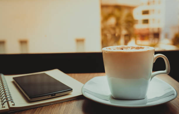 istock Capuccino coffee,notebook and mobile on wooden table the windows background 828489732