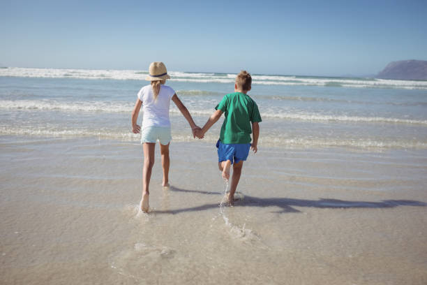 istock Rear view of siblings holding hands while running on shore 828493336