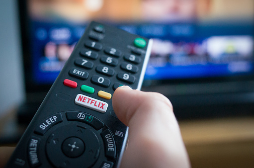 Southampton, England - July 31, 2017: Using a television remote control with dedicated Netflix button, TV in the background.