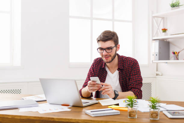 istock Young happy businessman in office using cell phone by the laptop 828513466