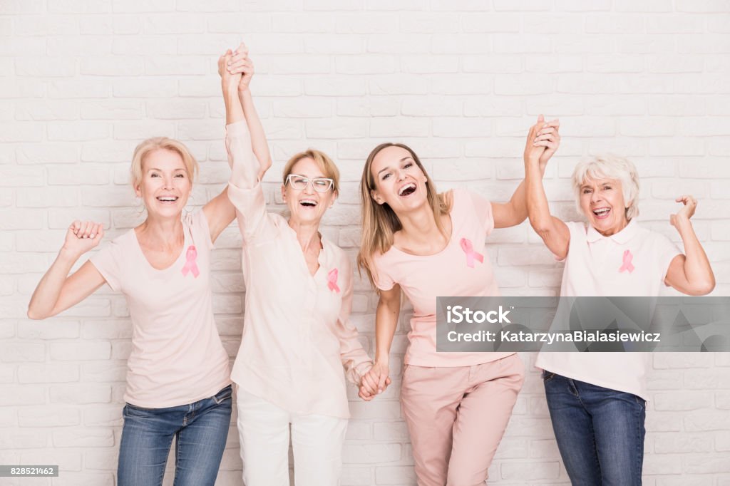 Group of ladies cheering Group of smiling ladies with pink ribbons cheering and holding hands Women Stock Photo