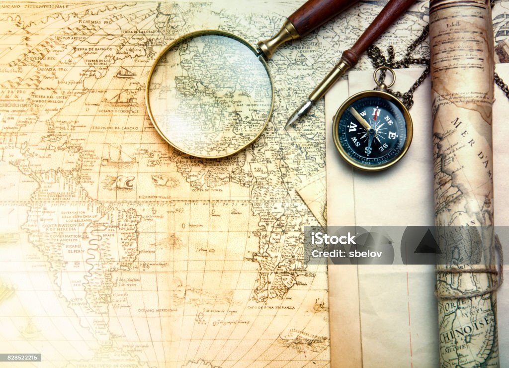 An brass compass on a old map background compass, magnifying glass and pen lying on an ancient world map Old Stock Photo