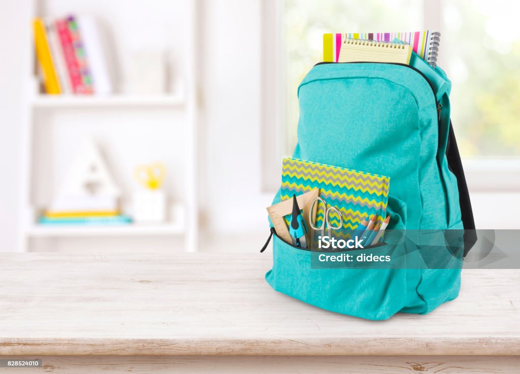 Backpack with school supplies on table over blurred educational interior Child Stock Photo