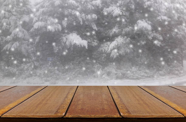 istock Blurred snowing in pine forest through glass window background with wood table. 828530988