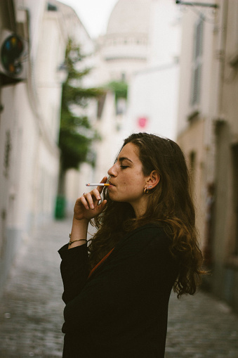 Young woman smoking in Montmartre, Paris with a view of the Sacre-Coeur behind the model.