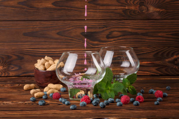 Two big glasses with fruit juice. Bilberries, raspberries, peanuts in a bowl, mint and on a dark brown wooden background.
