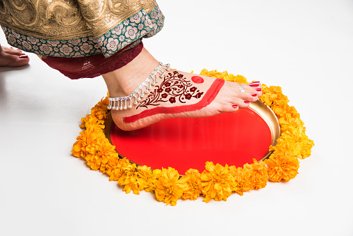 Gruha Pravesh / Gruhapravesh / Griha Pravesh, closeup picture of right feet of a Newly married Indian Hindu bride dipping her fit in a plate filled with liquid kumkum then stepping in husband's house