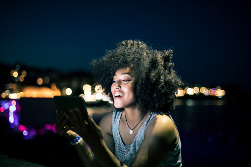 Cheerful african woman using digital tablet on beach at night.
