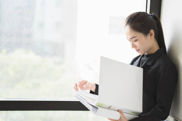 istock Asian Business woman holding document files beside a window 828642224