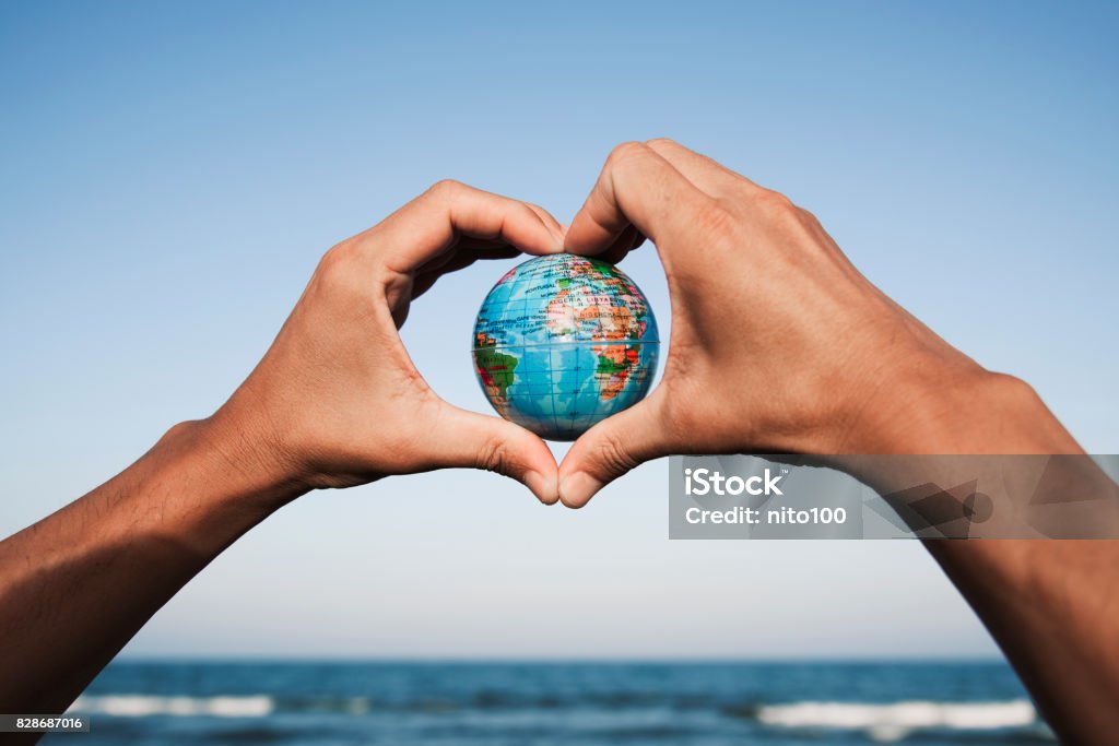 young man with a world globe in his hands closeup of a young caucasian man with a world globe in his hands forming a heart against the blue sky, in front of the sea Globe - Navigational Equipment Stock Photo