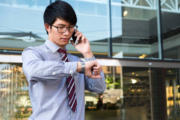 istock Executive in a hurry, businessman looking at his watch on hand, checking the time and using smart phone while standing on the office. outdoor background 828719386