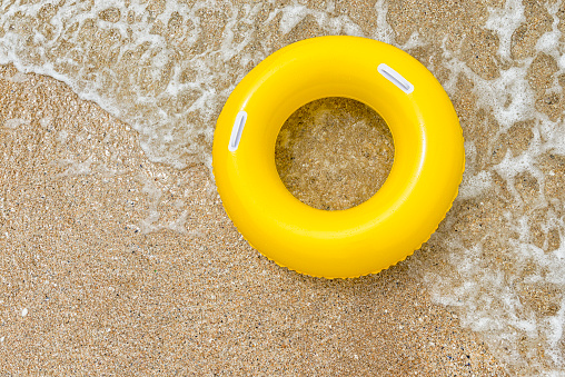 Yellow inflatable ring riding a wave at Pend Vounder Beach, South Cornwall on a bright June day.