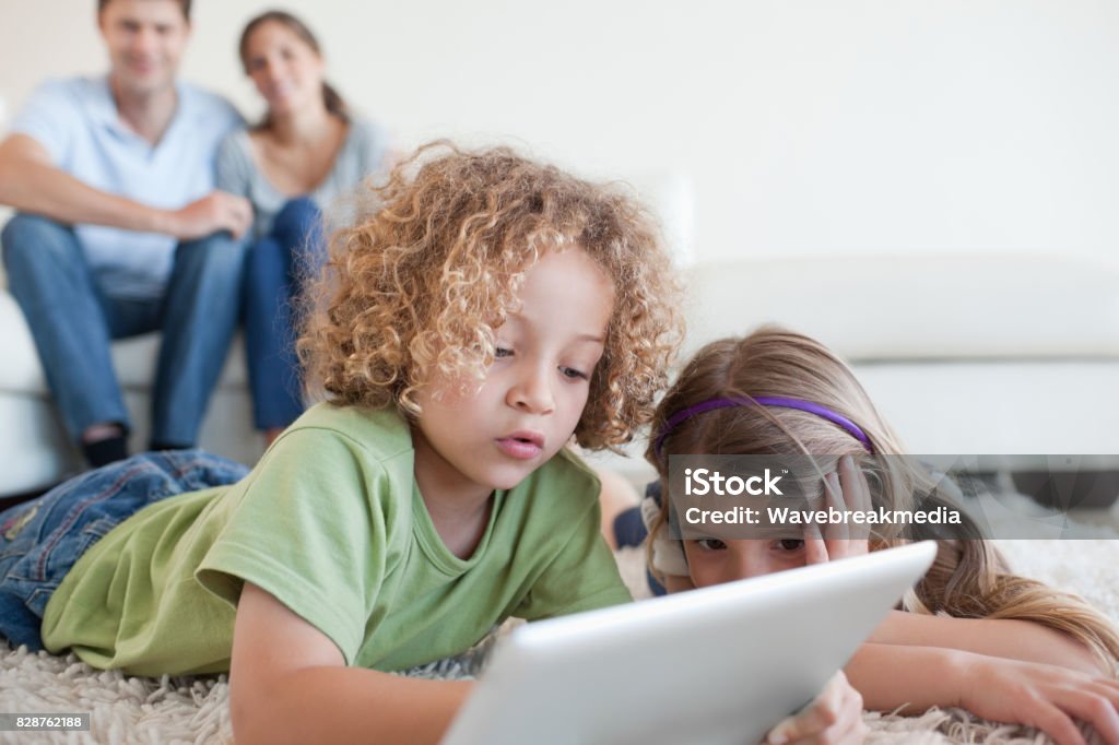 Young children using a tablet computer while their happy parents are watching Young children using a tablet computer while their happy parents are watching in their living room 20-29 Years Stock Photo