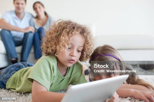 Young Children Using A Tablet Computer While Their Happy Parents Are Watching Stock Photo - Download Image Now